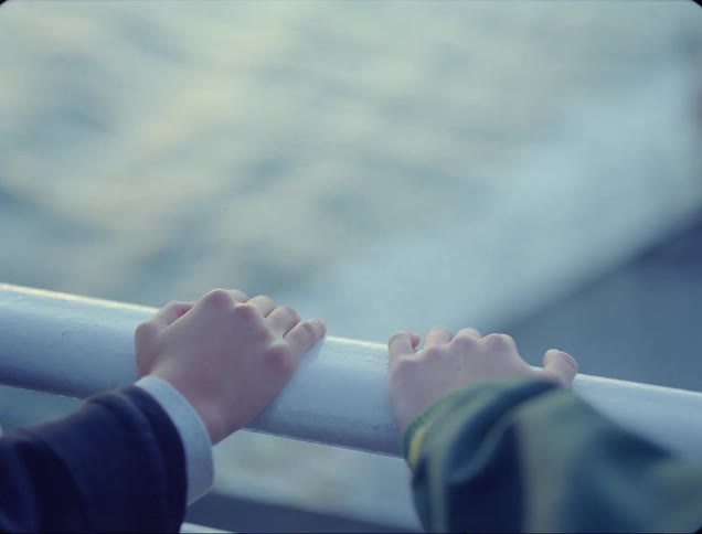 Two people move their hands together on the boat railing