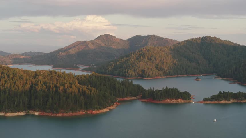 Forest trees cover hills all the way down to the curving coast with boats on serene water