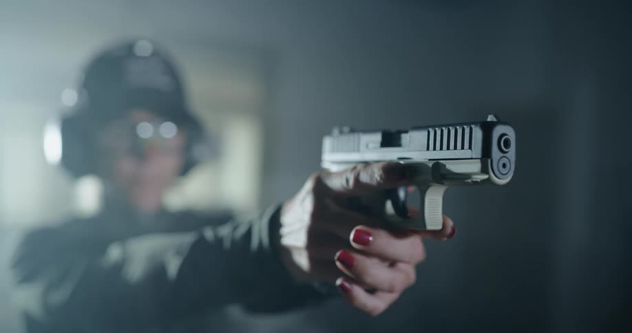 A woman with a hat ear muffs and goggles standing in a room and pointing a gun