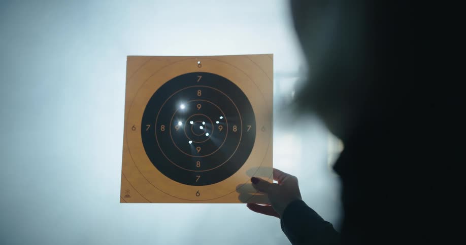 A woman holds a paper shooting target up to the light to clearly see the bullet holes within it