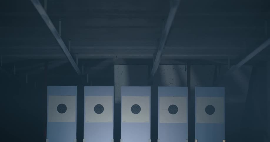 A row of panels with shooting targets mounted on the front suddenly turn to face the camera in a dimly lit shooting range
