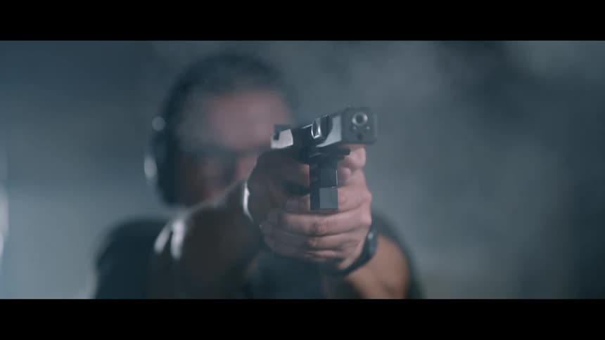 Smoke billows and bullets go flying as a man fires a handgun at a shooting range