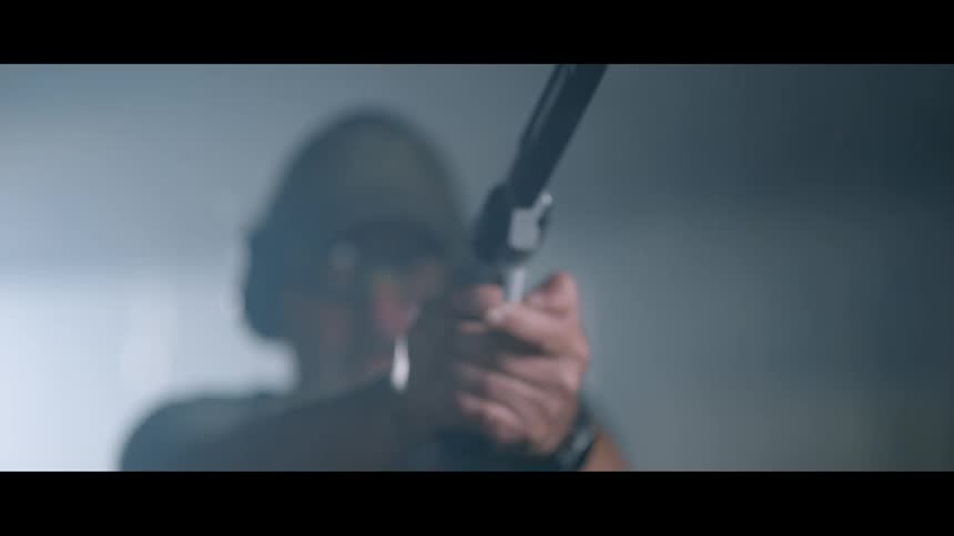 A man in safety equipment fires a pistol in a dimly lit room