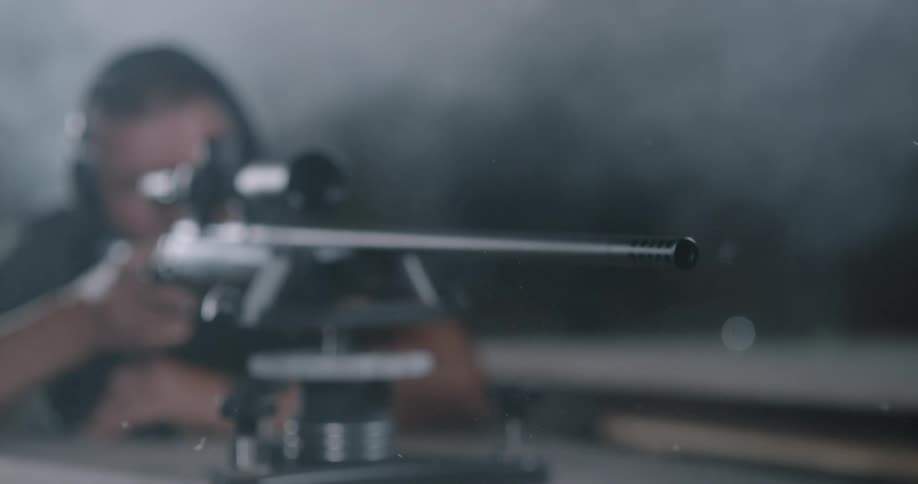 A man fires a rifle mounted on a surface in a smoky shooting range