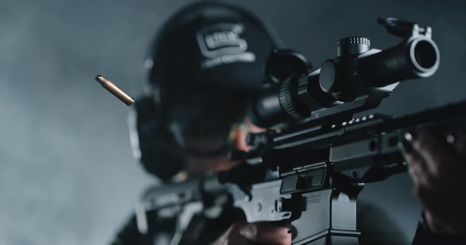 A woman in personal protective gear fires a rifle causing the casing of an expended bullet to be ejected into the air