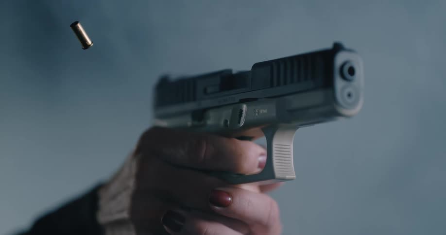 Person wearing red fingernail polish pulls trigger firing gun that ejects casing into air