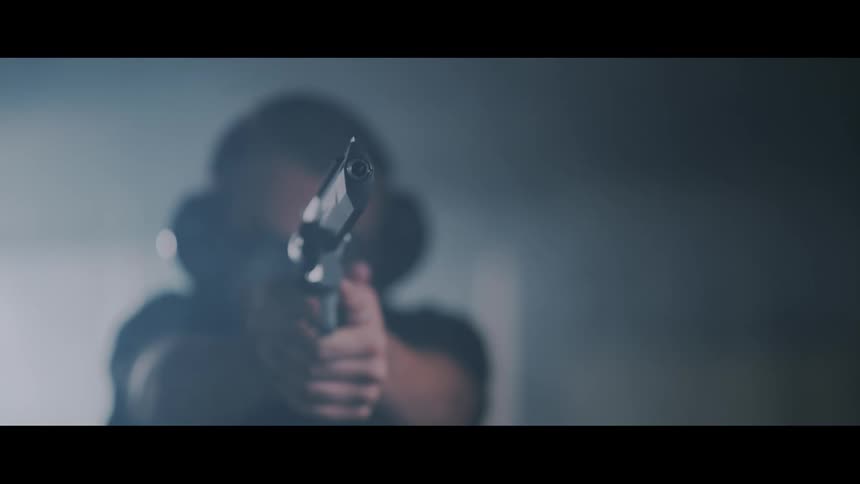 A man fires a pistol in a dim room filled with gunsmoke