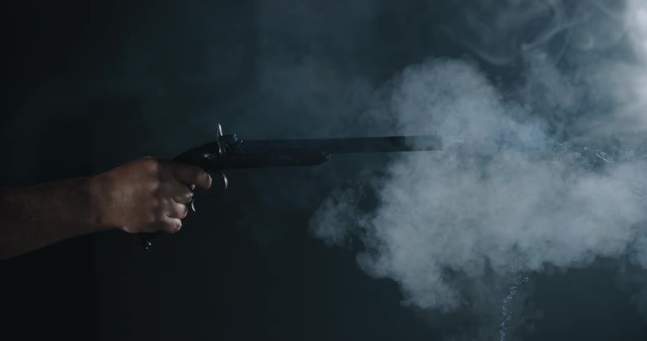 A man fires an old pistol in a dark room