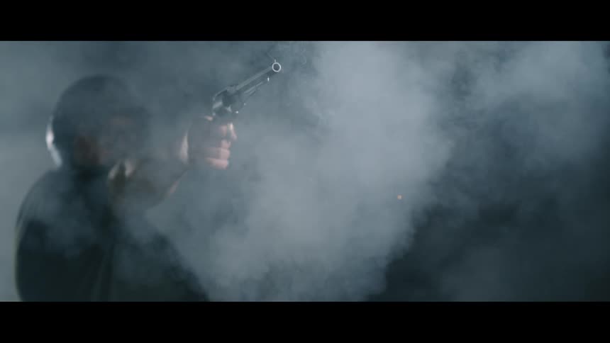 A man wearing earmuffs holds and fires a pistol causing smoke and sparks