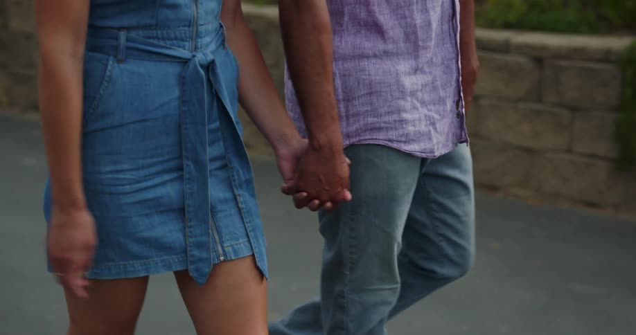 A man and woman walking and holding hands with trees in the background