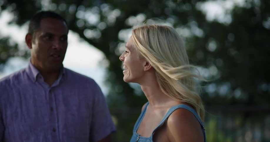 Man and woman stand outdoor holding wine glasses laughing and talking
