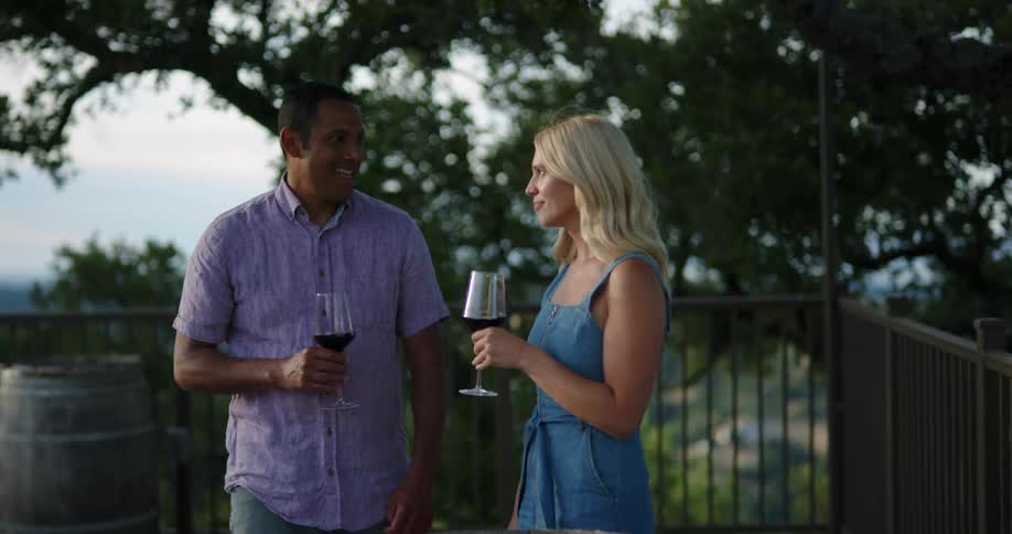 A man and woman talk and laugh while drinking wine outdoors during the day