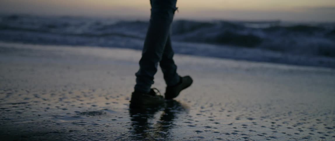 A person slowly walks towards the water at sunset