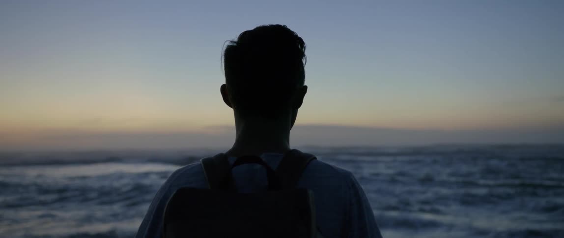 A man looks out at the waves on a beach at dusk