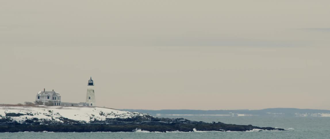 A lighthouse sits on a rugged wintery coastline in Maine
