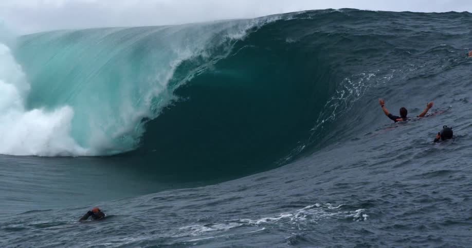 People in the ocean with cameras taking pictures of a wave with the sky and clouds in the background