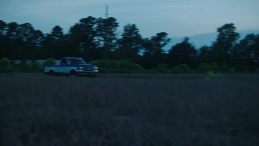 Truck drives along road past field as red sky shows on horizon