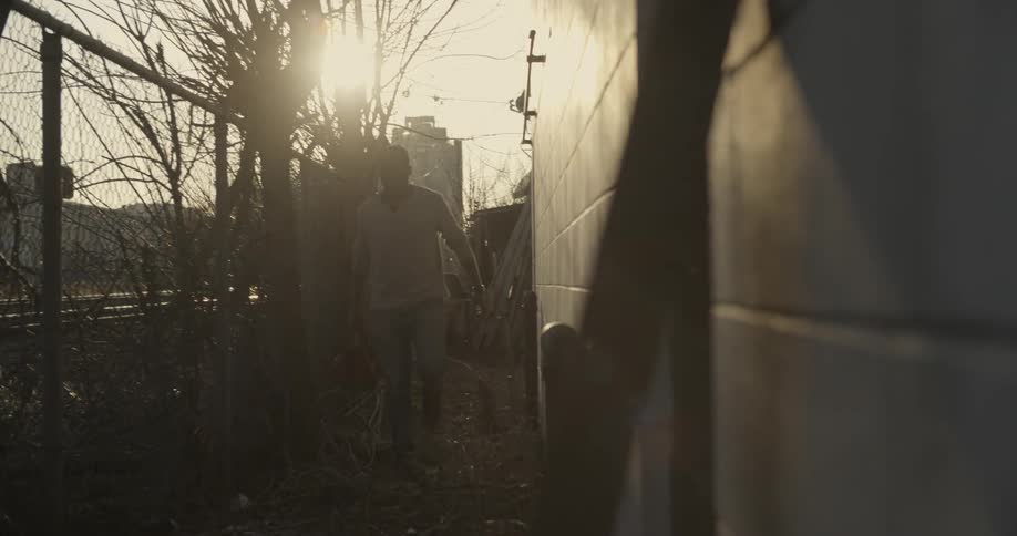 A man walks between a fence and a building