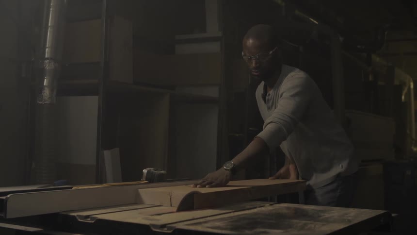 A man is cutting a board on a table saw