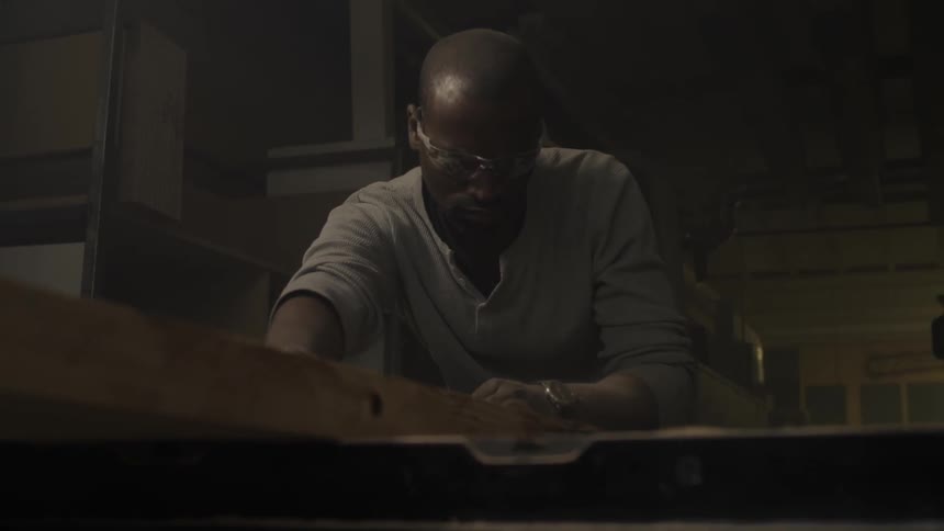 A man is cutting a board on a table saw