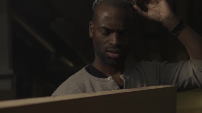 A man blows saw dust off a plank of wood