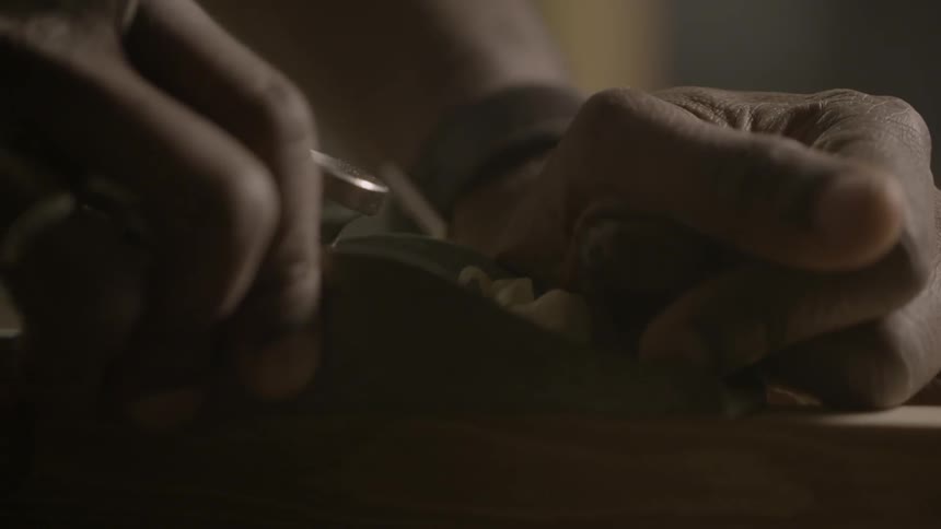 Two hands using a tool to shave wood