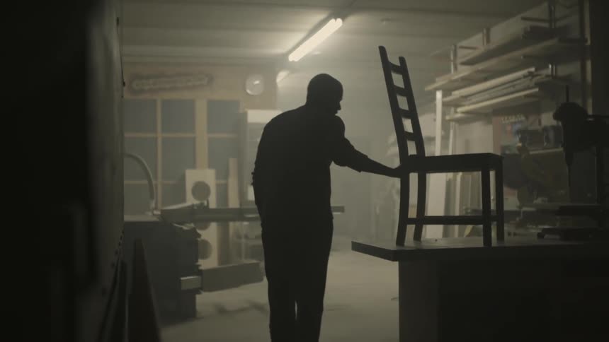 Man sets a chair on a work table and then leaves the room