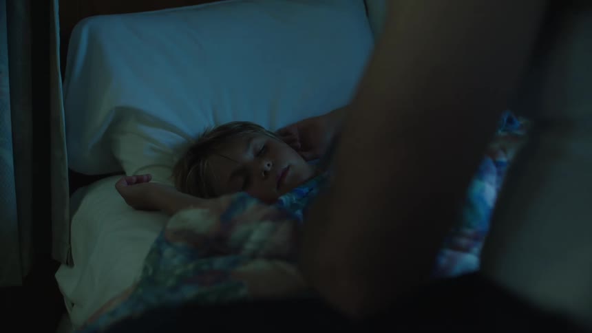 A small boy being tucked into bed as he sleeps