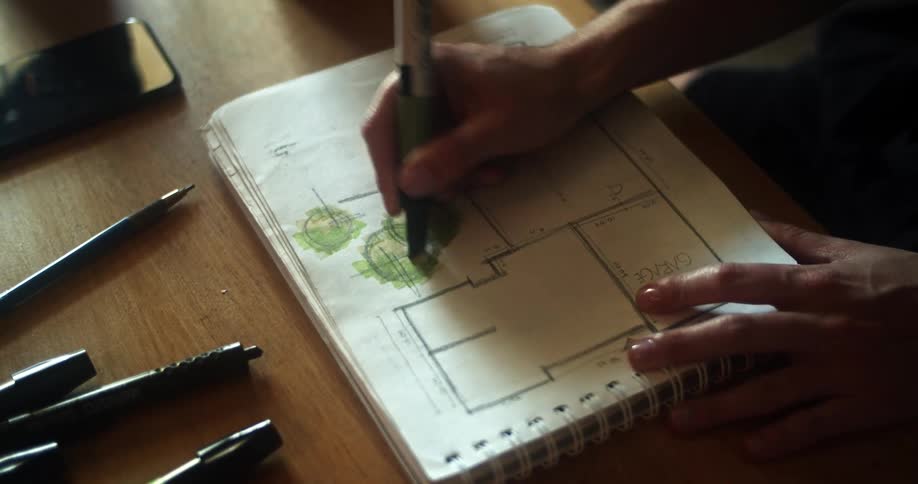 A person is drawing in trees onto a drawing of a floor plan of a building