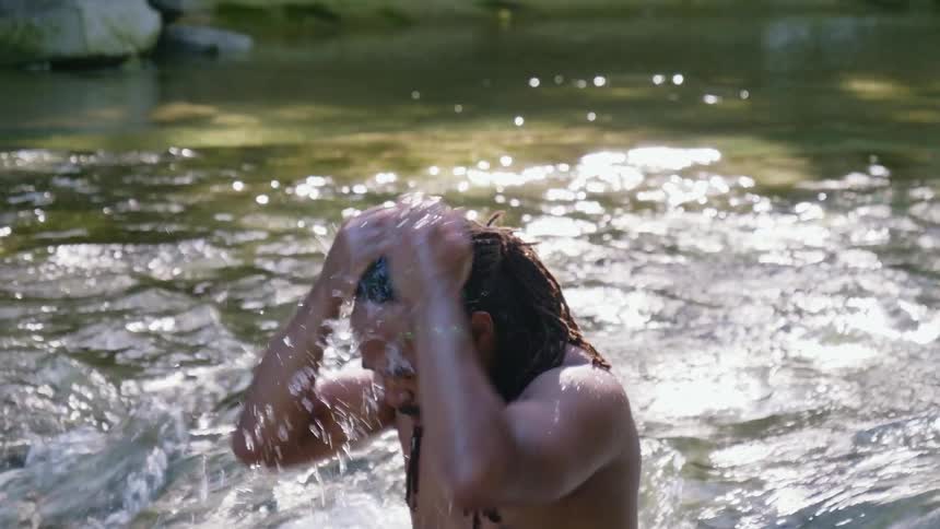 A man splashes water on his hair and face while standing in a river