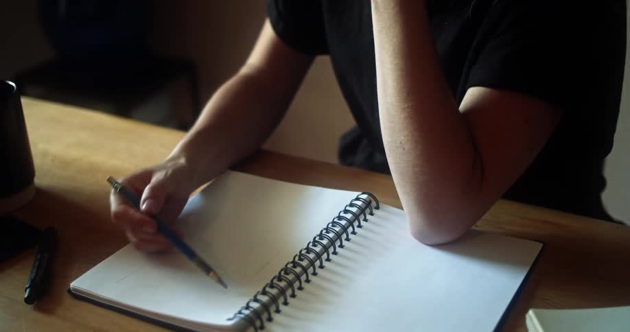 A woman sits at a desk and sketches in a book