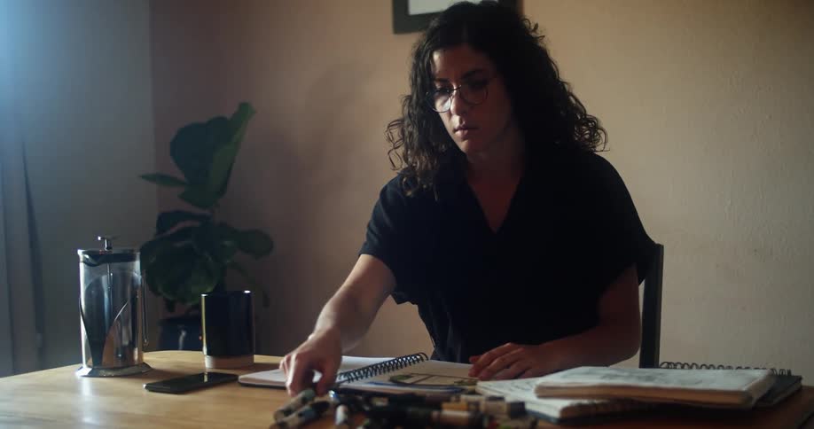 A woman sits at her desk and picks up a marker and starts to write in a notebook