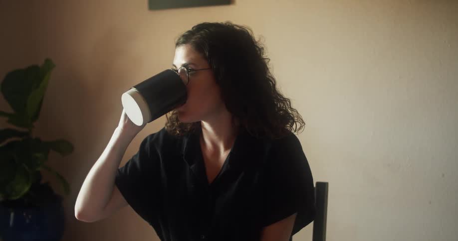 A woman sitting at a desk drinks from her mug