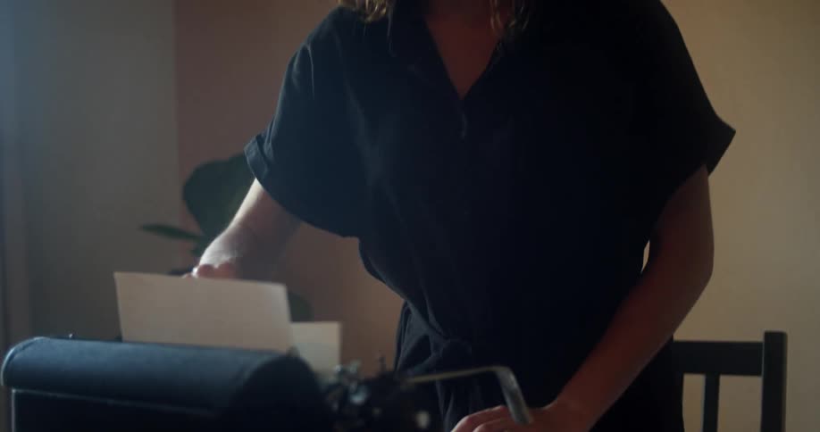 A woman at home pulls a piece of paper out of a vintage typewriter and stands up