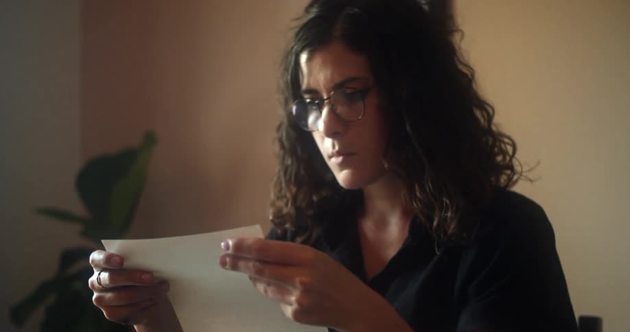 Female sitting in front of a vintage typewriter removes the piece of paper from the machine while reading the typed written text then stands up and turns to walk away