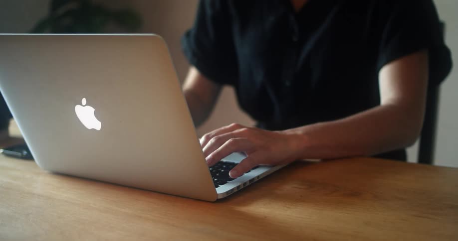 Female sitting a kitchen table in front of a laptop types quickly while concentrating and looking down at her hands