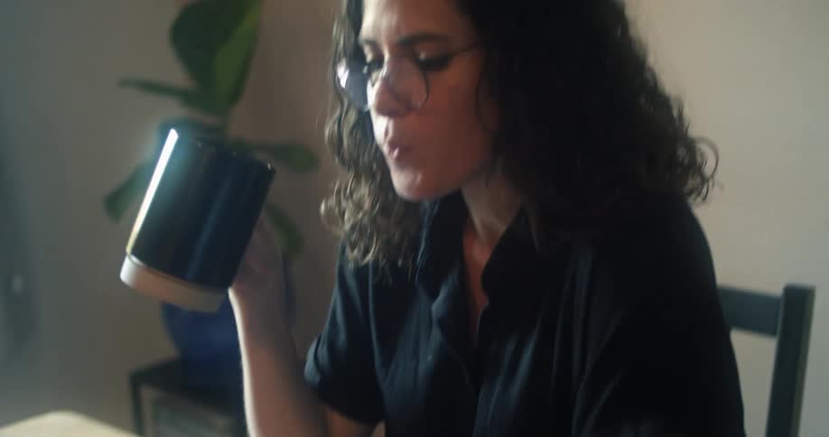 A woman drinks coffee while using her laptop at home