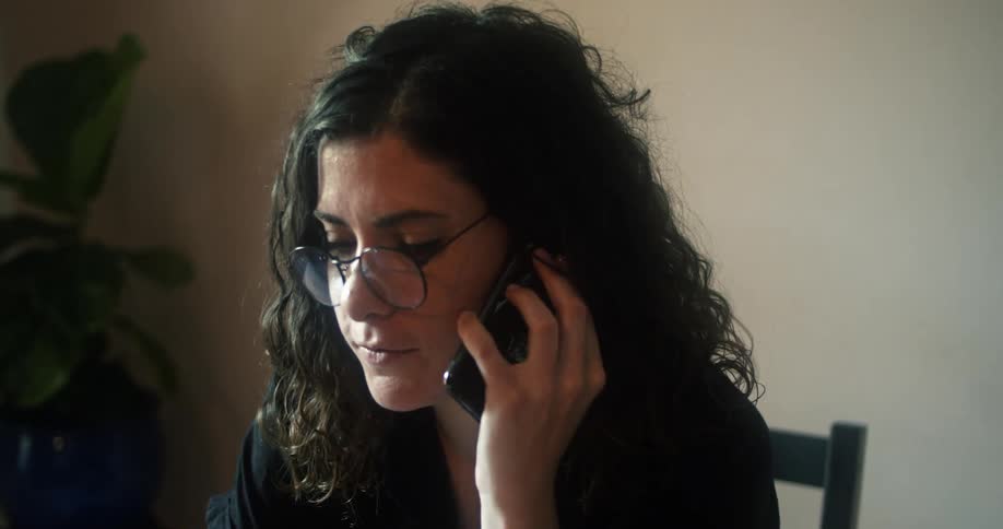 A woman answers the phone while sitting at home and using her laptop