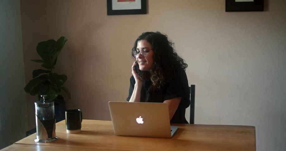 A woman typing on a laptop pauses to answer a phone called before returning to her typing