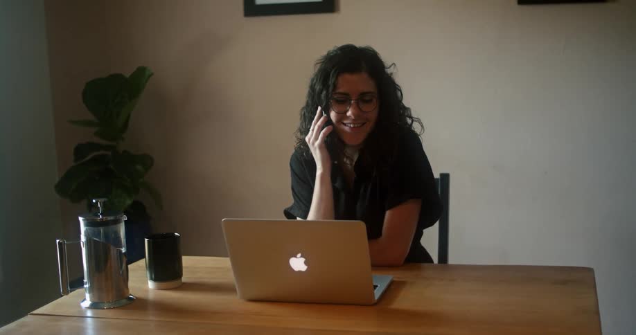 A woman sits at a desk with a laptop and takes a phone call