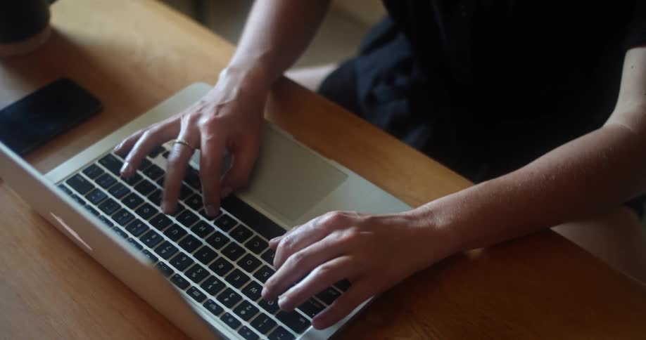 A person in black clothing types on a laptop keyboard using their forefingers and thumbs