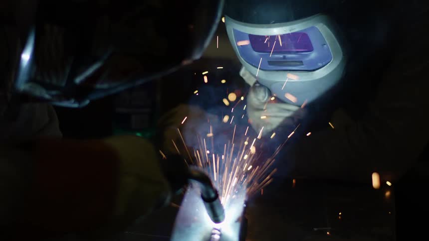 Two welders work on a piece of metal