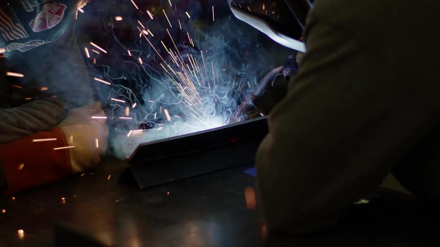 A person with a torch and a welding mask welding with smoke and sparks