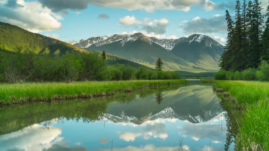 A river surrounded by grass with a mountain range the sky and clouds in the background