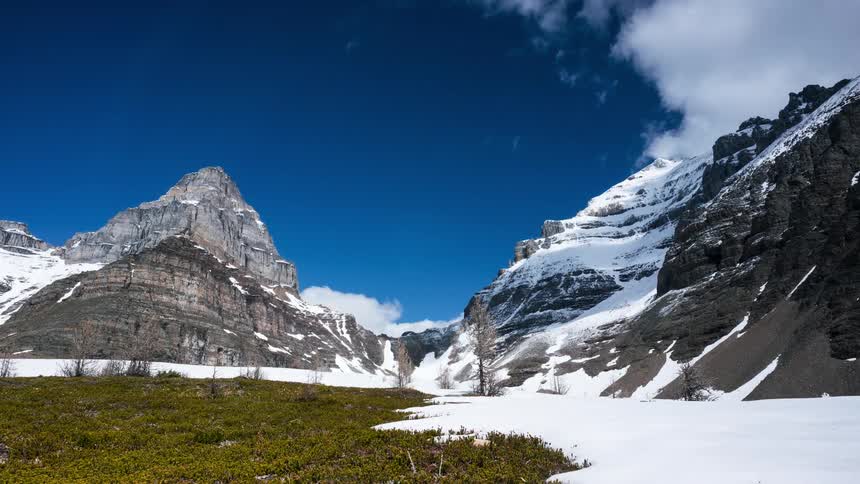 Time lapse of clouds on a blue sky running over the summit of a snow covered mountain range
