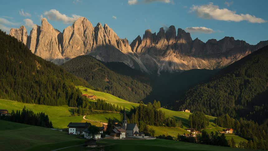 Time lapse of a small rural community that sits in a valley forest with a rocky mountain ridge in the background