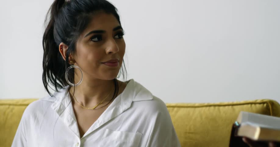 A young woman sitting on a couch turns her head and smiles