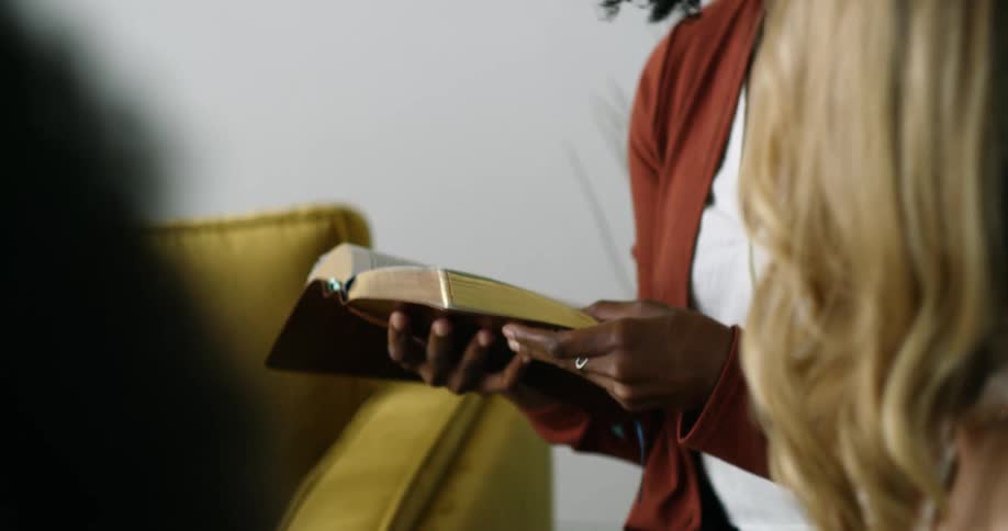 A woman reads from a book as two other women sit and listen