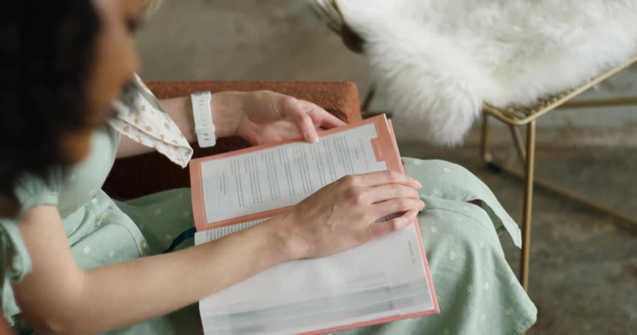 A woman in a pale green dress reads a book while sitting in a chair