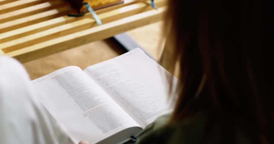 A white woman reads a book and marks a page with a blue ribbon